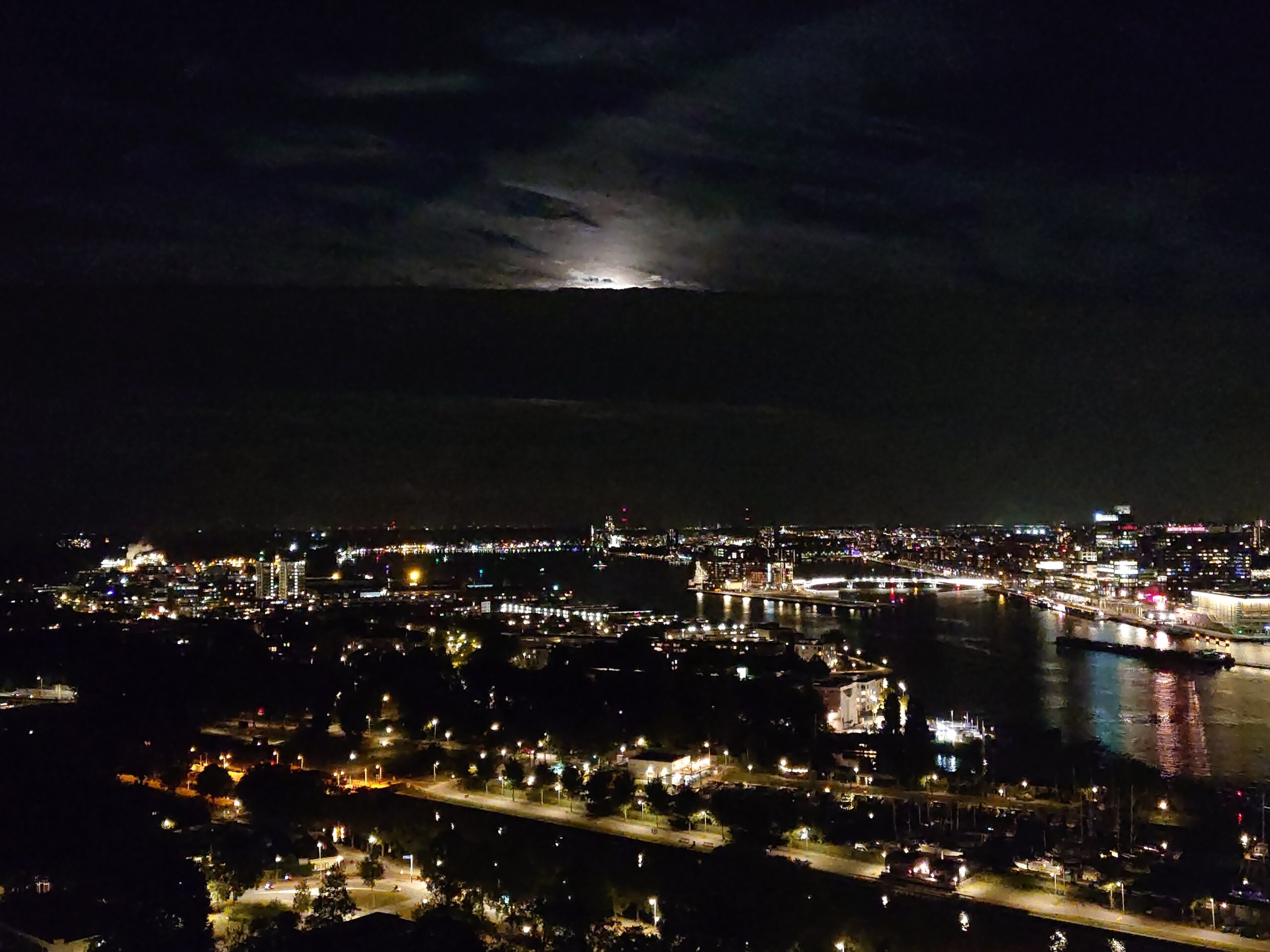 雲を突き抜けて昇るハーベストムーンとアムステルダムの夜景