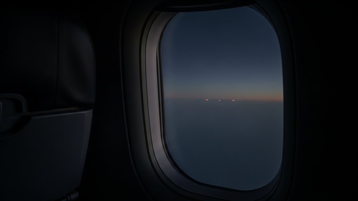長時間フライトの機内から見える夜明け前の空。価値判断の軸足について考える時間を象徴するイメージ。